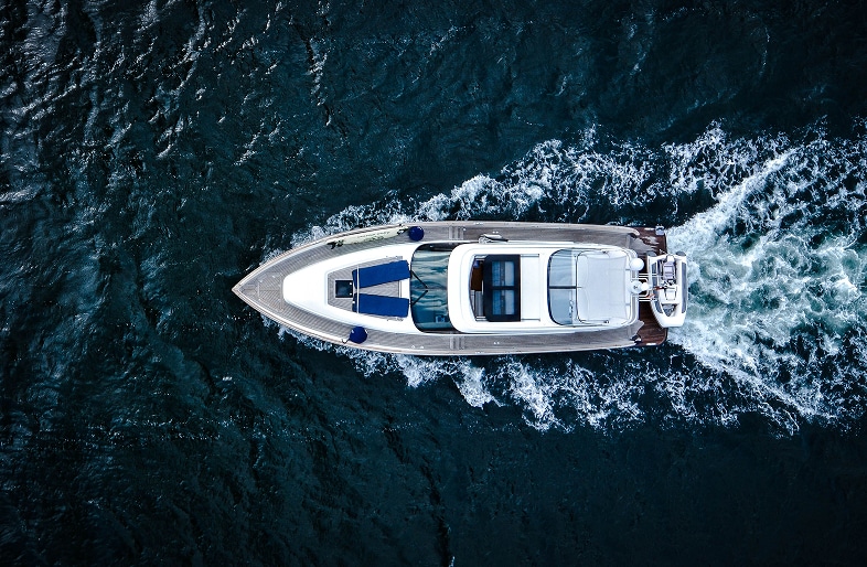 Aerial view of a white luxury yacht moving quickly through dark blue water, leaving a white wake behind it. The boat’s deck and sleek design are clearly visible—reminding us to stay safe and aware of boating accidents, as Massaro Law advises.