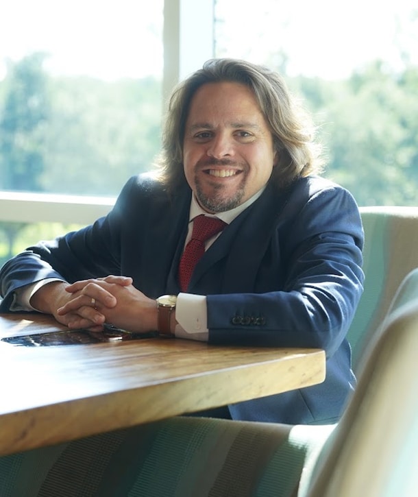 Vincent Massaro, personal injury attorney at Massaro Law, sitting at a wooden table with hands clasped, wearing a blue suit and red tie.